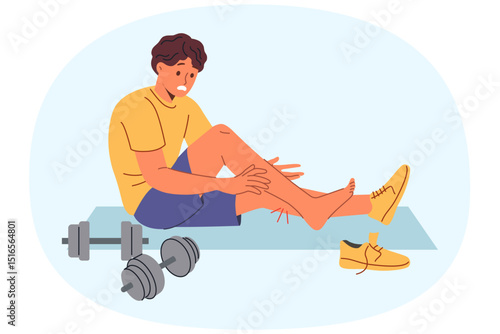Injured sportsman sits on mat for sports and gymnastics near dumbbells, after stretching muscles on legs. Injured athlete experiences pain and agony after careless use of sports equipment