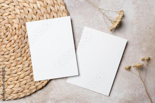Two blank white vertical wedding invitation cards, front and back sides on beige background with dried flowers and woven placemat. Boho style flat lay with copy space