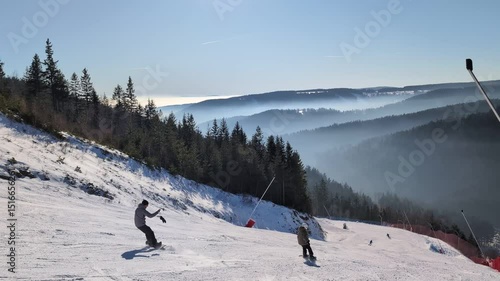 Skiers speed down a snow-covered slope surrounded by woods in winter - view from the hilltop