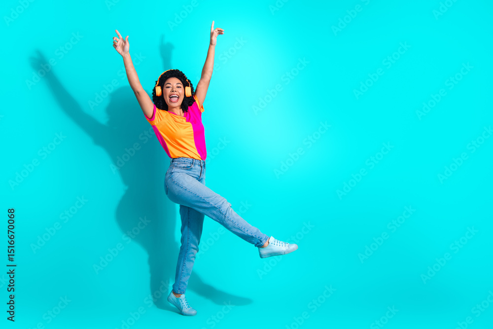 Young woman dancing joyfully in casual outfit on teal background, wearing headphones and expressing cheerful happiness Young woman dancing joyfully in casual outfit on teal background, wearing headphones and expressing cheerful happiness