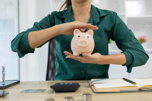 A woman is planning to save money. She puts coins in a piggy bank and records her savings in her notebook. The concept of saving money and being financially responsible.

