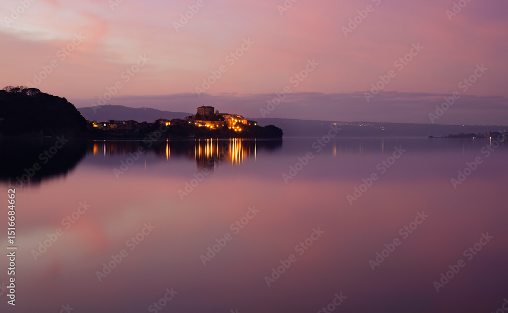 Naklejka premium Sunset over Lake Bolsena paints the sky with warm hues, reflecting on tranquil waters. A serene Italian landscape perfect for travel, nature, and romantic visual themes. Peaceful and captivating views