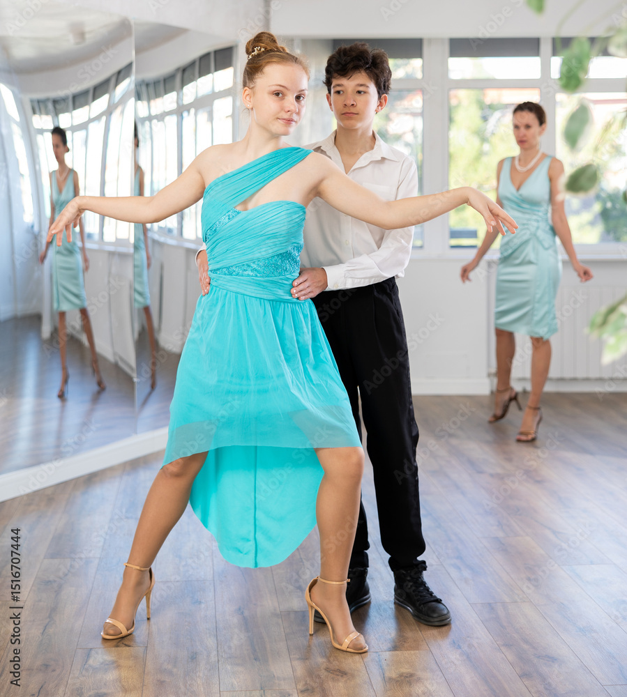 Naklejka premium Passionate teen dancers, girl and boy practicing ballroom dancing in dance studio, gracefully performing waltz while female trainer monitoring technique and progress..
