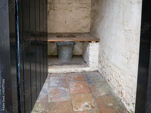 Tablou pe pânză Rustic outdoor latrine toilet with wooden bench and metal bucket.