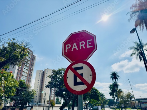Placa de sinalização com proibido estacionar e pare com fundo de predios urbanos.