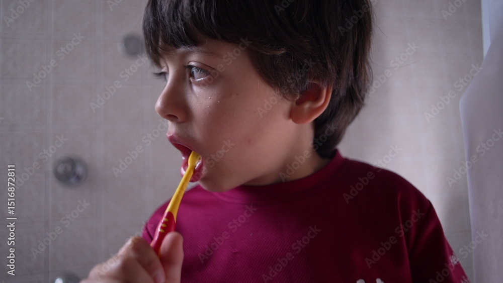 Boy brushing teeth in bathroom, looking to the side, everyday routine, close-up view, dental care in progress, thoughtful expression, simple home setting Boy brushing teeth in bathroom, looking to the side, everyday routine, close-up view, dental care in progress, thoughtful expression, simple home setting