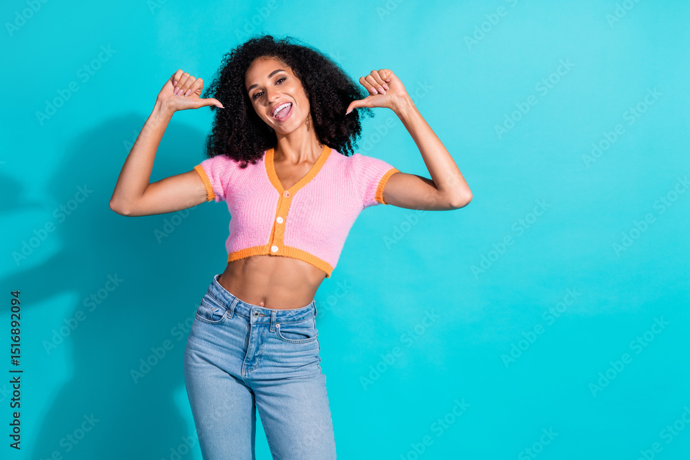 Fototapeta premium Cheerful young woman in trendy pink top and jeans smiles confidently against a bright turquoise background