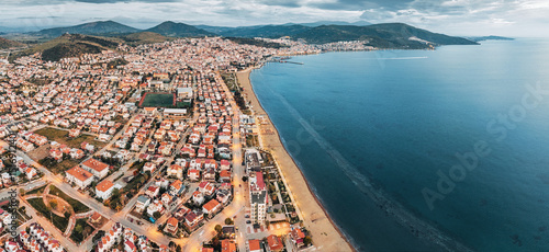 Fototapeta Naklejka Na Ścianę i Meble -  Drone capturing a panoramic view of a Dikili, Turkiye coastal cityscape at twilight, with illuminated streets, residential buildings, and sandy beach