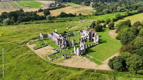Aerial view of ancient ruins of castle acre priory with stone walls and grassy surroundings. The structure features remnants of arches and towers, set in a lush green landscape with fields.