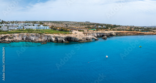 Wallpaper Mural Rugged limestone cliffs with Love arch caves along the Ayia Napa shoreline, turquoise Mediterranean waters, and modern houses in a rocky, sparse landscape. Torontodigital.ca