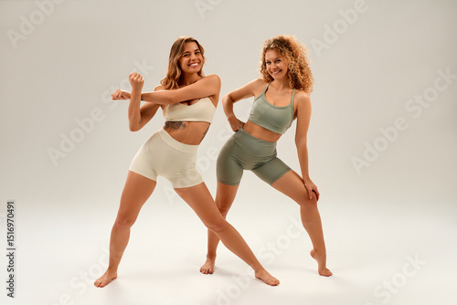 Two young women in activewear doing fitness stretches, strength and wellness training concept
