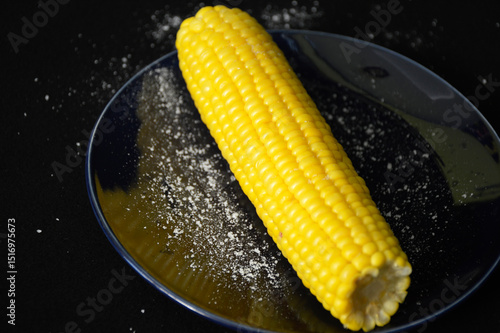 Foto heads of boiled corn and grains of salt on a dark plate
