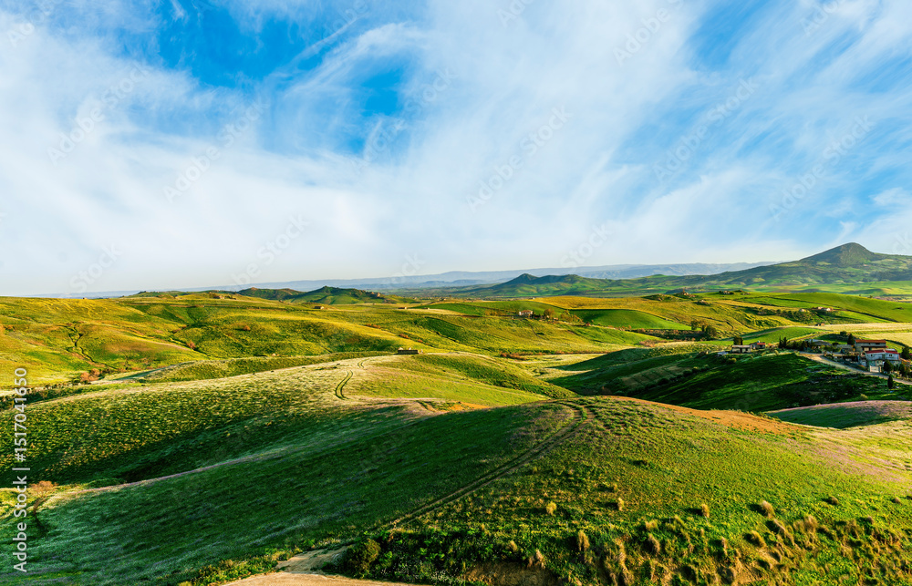 Obraz premium green agricultural spring or summer landscape of grassland hills near small village with young grass and amazing cloudy sky