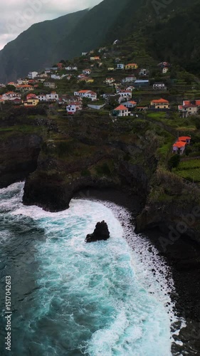 Breathtaking aerial drone footage showing dramatic cliffs on the tropical island of Madeira. The rugged coastline meets the Atlantic Ocean, revealing lush greenery and steep rock formations.