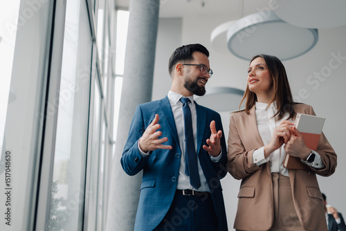Businesspeople discussing work while walking in office hallway