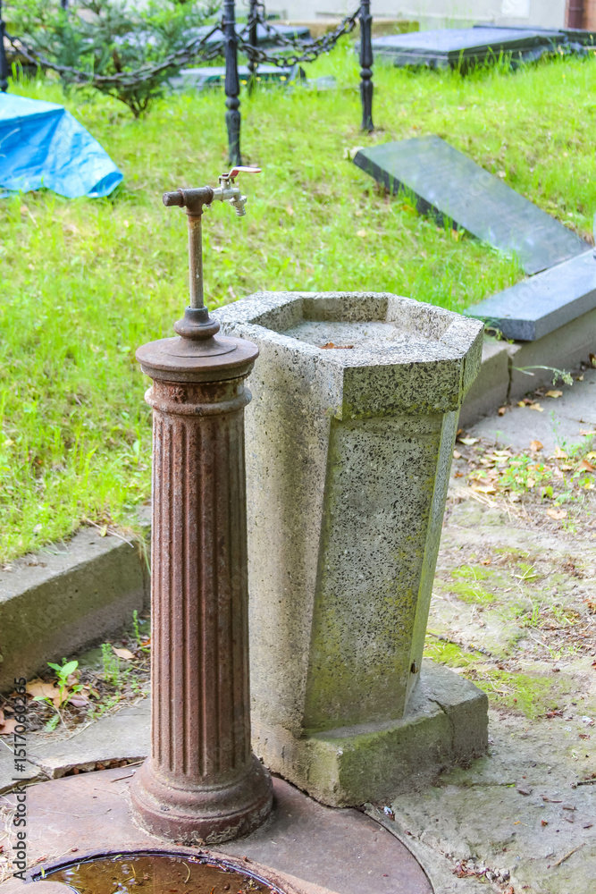 Fototapeta premium Stone water well with vintage hand pump showing traditional cemetery utility infrastructure and historic craftsmanship