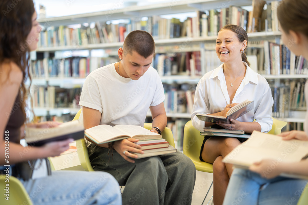 Group of female and male students reading books and talking on chair in library Group of female and male students reading books and talking on chair in library