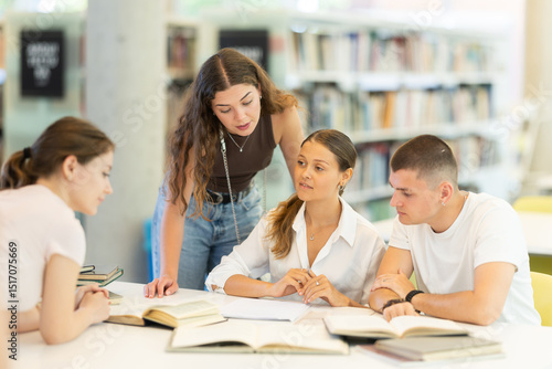 Group of students talking, reading books and taking notes at table in library
