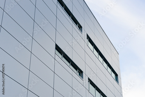 The exterior wall of a contemporary commercial style building with aluminum metal composite panels and glass windows. The futuristic building has engineered diagonal cladding steel frame panels.