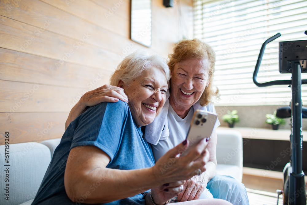 Obraz premium Senior lesbian couple laughing while looking at smartphone after home workout