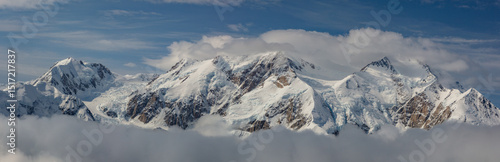 The snow capped Alaska Range mountains surrounded by clouds.  This Alaskan mountain panorama was captured from the air on a glacier landing tour out of Talkeetna Alaska.