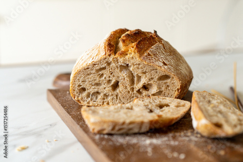 Crispy sourdough bread sits beside a glass jar filled with active starter, accompanied by a rustic cloth and a wooden board in a warm kitchen atmosphere.