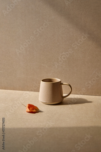 Earthy beige mug with a small piece of fruit on a neutral surface