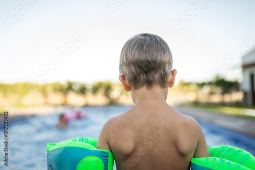 Little boy standing by the pool with floaties, about to jump in