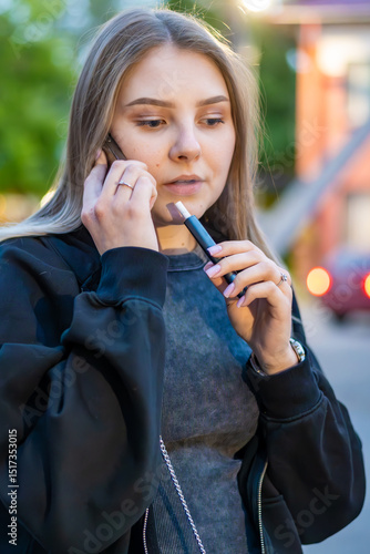Wallpaper Mural Young woman smoking e-cigarette talking on the phone in the street. Addiction concept. High quality photo.	 Torontodigital.ca