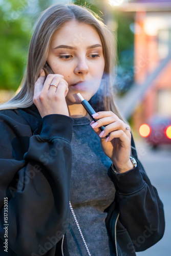 Wallpaper Mural Young woman smoking e-cigarette talking on the phone in the street. Addiction concept. High quality photo.	 Torontodigital.ca