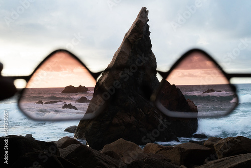 Hand holding glasses up against sea with rock 