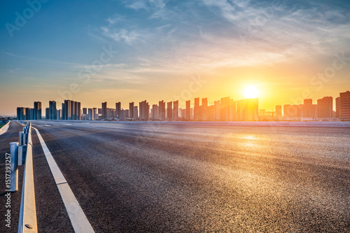 Fototapeta Naklejka Na Ścianę i Meble -  Empty asphalt highway road and modern city skyline with residential area buildings at sunset