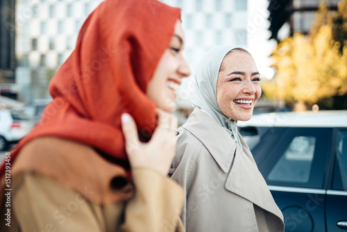 Two smiling young muslim businesswomen walking in the city