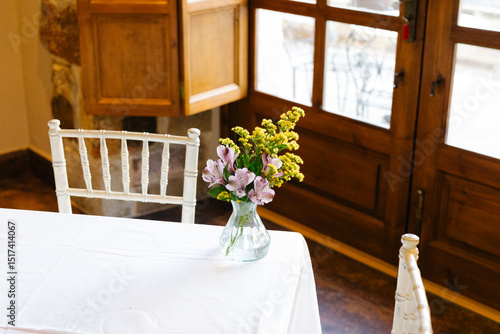 Vase decorated with wild flowers placed in the corner of a table photo