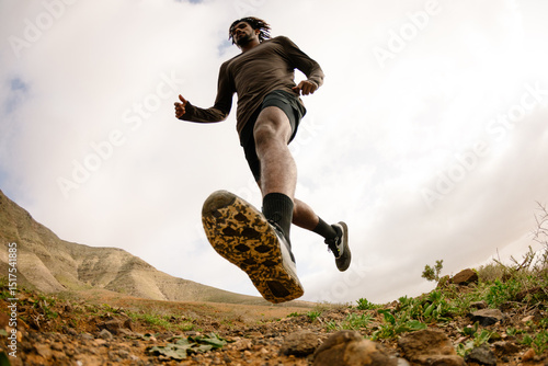 Wide shot from low angle of a runner crossing a rocky trail