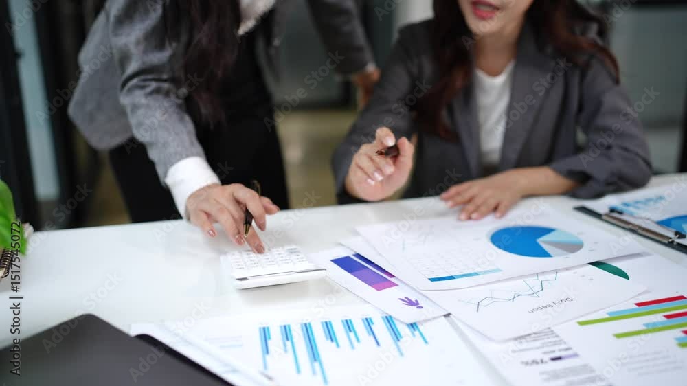 Two Asian businesswomen sit in an office, with graph paper on their desks, calculating investment plans. Two Asian businesswomen sit in an office, with graph paper on their desks, calculating investment plans.