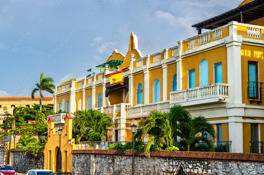 Naklejka premium Vibrant colonial building with white columns and balconies stands in the historic district of Cartagena, Colombia, its bold orange facade glowing under a bright blue sky and tropical sunlight