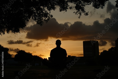 Person meditating at sunset in an urban park surrounded by trees and buildings