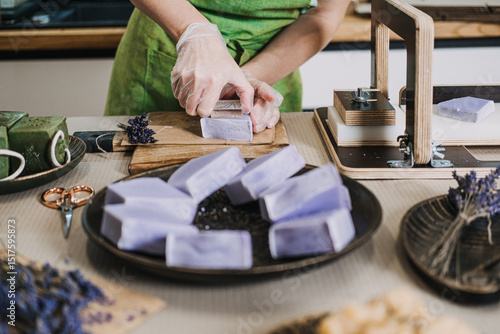 Slika na platnu Person slices lavender soap bars by hand in a home soap studio filled with artisan tools and natural ingredients