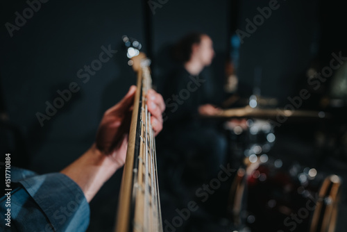 Fototapeta A detailed shot focusing on a guitarist's hand on the fretboard, with a drummer performing in the background, suggesting a lively band practice or music studio environment