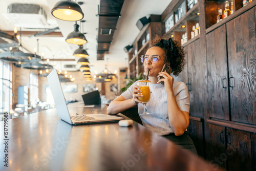 Portrait of a multicultural freelancer sitting in cafe and drinking juice while talking on cellphone.