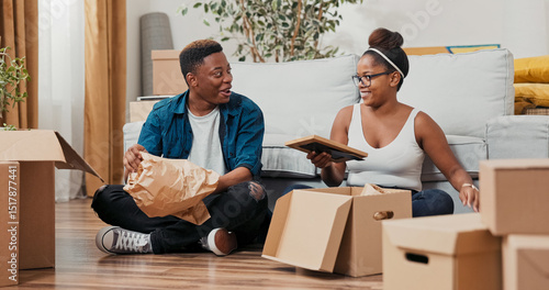 A husband and wife unpack boxes in their flat, sitting close on the floor. They reveal a framed picture, a fragile vase, and sentimental objects wrapped in packing paper.