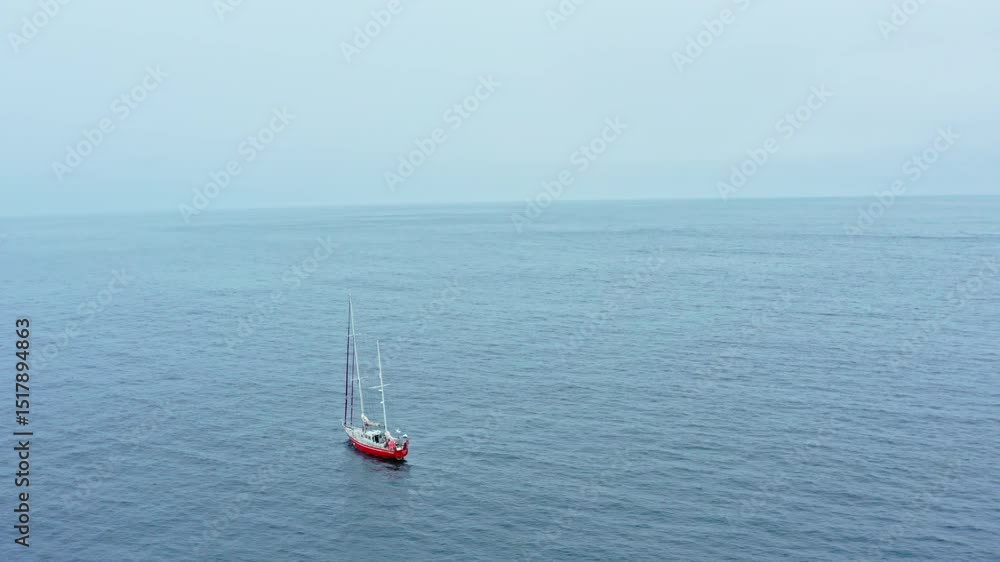 Solo sailboat drifts across open Beagle Channel in calm weather under a light blue sky, aerial orbit Solo sailboat drifts across open Beagle Channel in calm weather under a light blue sky, aerial orbit