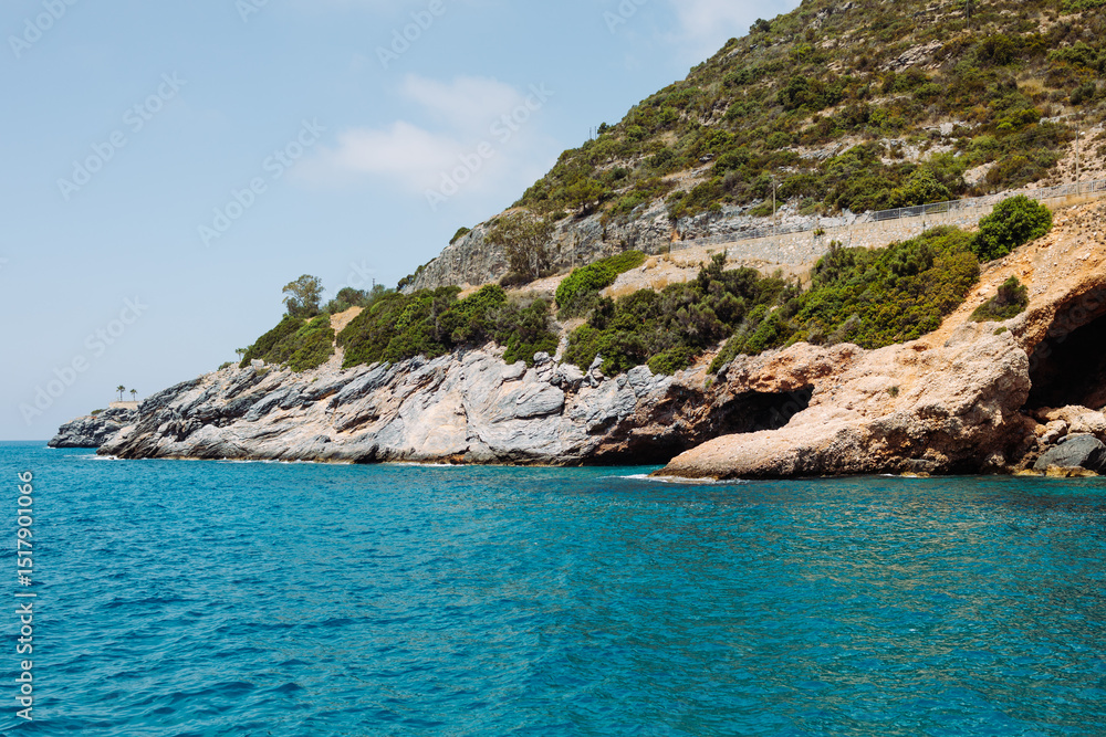 Fototapeta premium Sea cave in a rocky shore with turquoise transparent water. Picturesque natural landscape with rough texture of stones and deep entrance to the grotto. Ecotourism. Fascinating seascape.