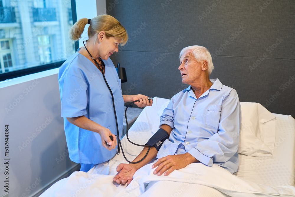 Fototapeta premium Nurse taking blood pressure of elderly man in hospital bed