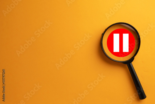 Obraz na plátně Magnifying glass focusing on a red pause button icon with white bars