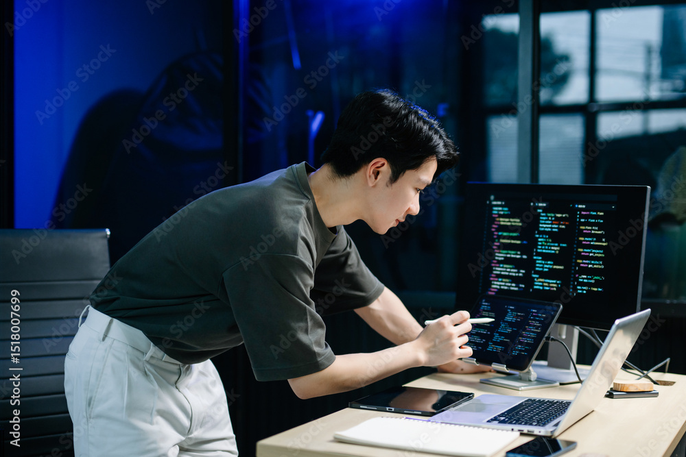 Young male programmer working with tablet and screen displaying code. Modern tech office setup, great for software, coding, IT.. Young male programmer working with tablet and screen displaying code. Modern tech office setup, great for software, coding, IT..