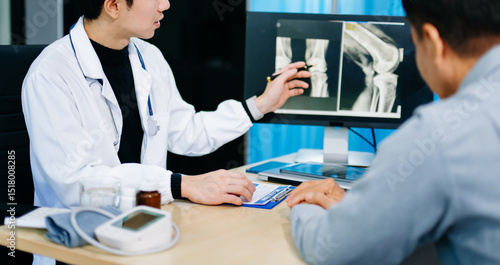 Canvastavla Asian doctor discusses knee X-ray results with senior patient in modern clinic