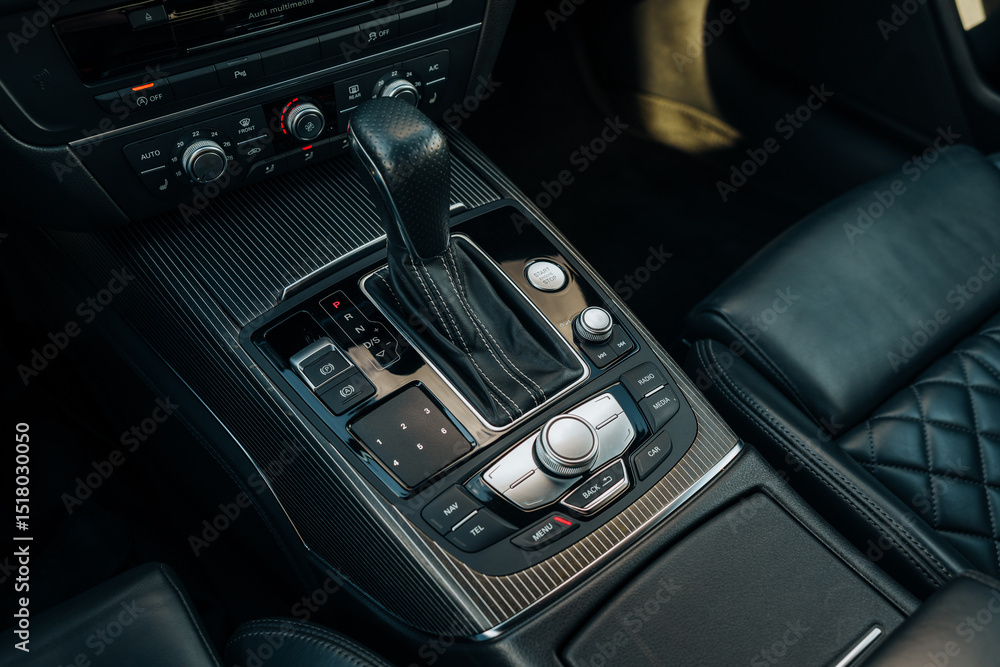 Obraz premium The photo shows the center console, buttons and the automatic sports transmission lever. Black premium leather, steering wheel. Luxury car interior design. Marketing, advertising or press articles.