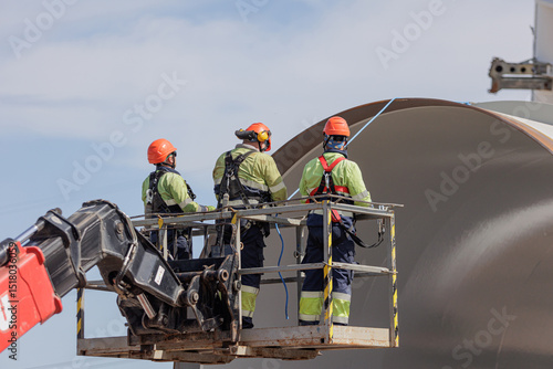 Construction workers wearing safety gear on an aerial lift platform at an industrial building site.